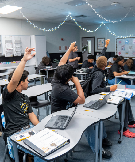 classroom of high school students with their hands raised